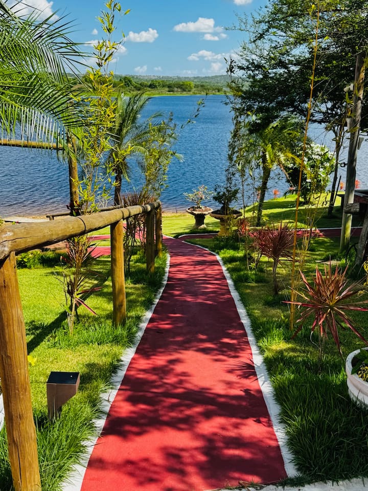 Caminho de jardim entre gramado e árvores, levando ao rio