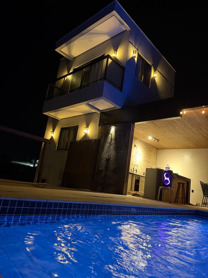 Prédio das suítes iluminado à noite, ao lado da piscina